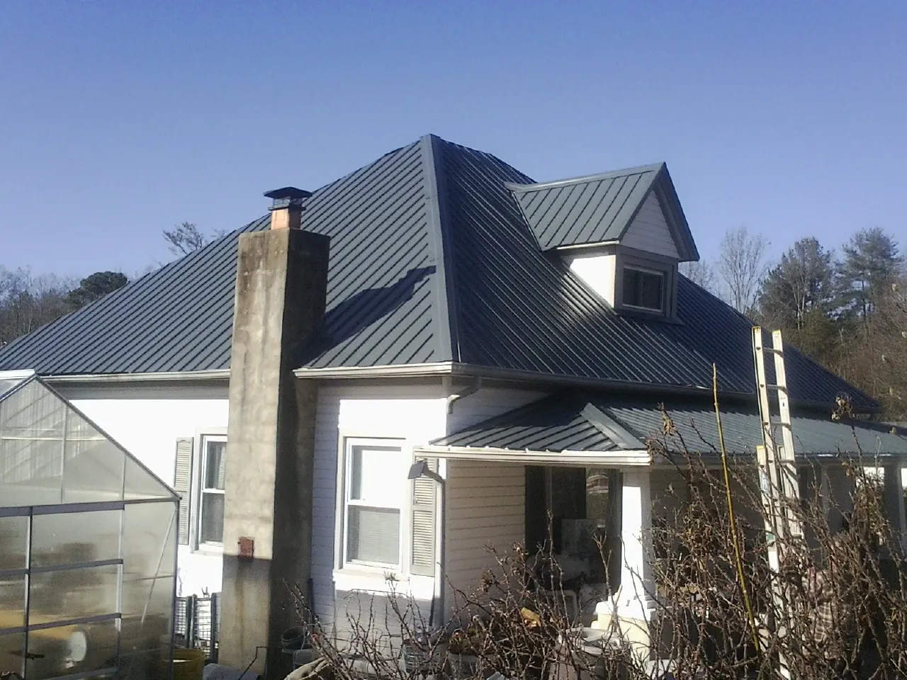 Dark blue standing seam metal roof on a white farmhouse with dormer — Slate & Tile Roof Repair by Roofing Brothers in Abrams