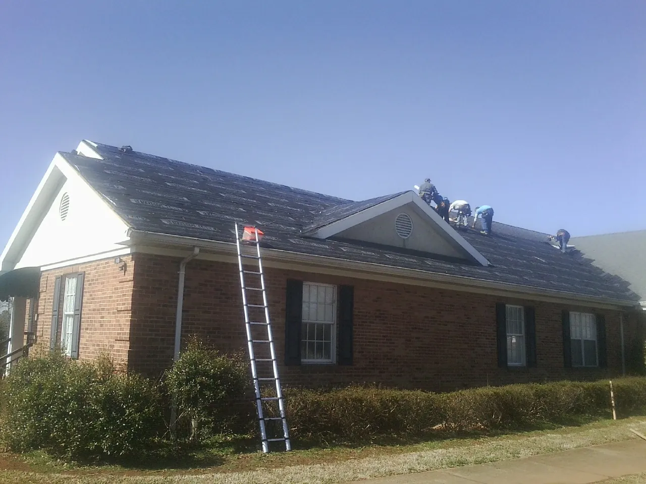 Crew tearing shingles off a brick ranch roof with a ladder set — Metal Roof Repair work by our crew in Abrams