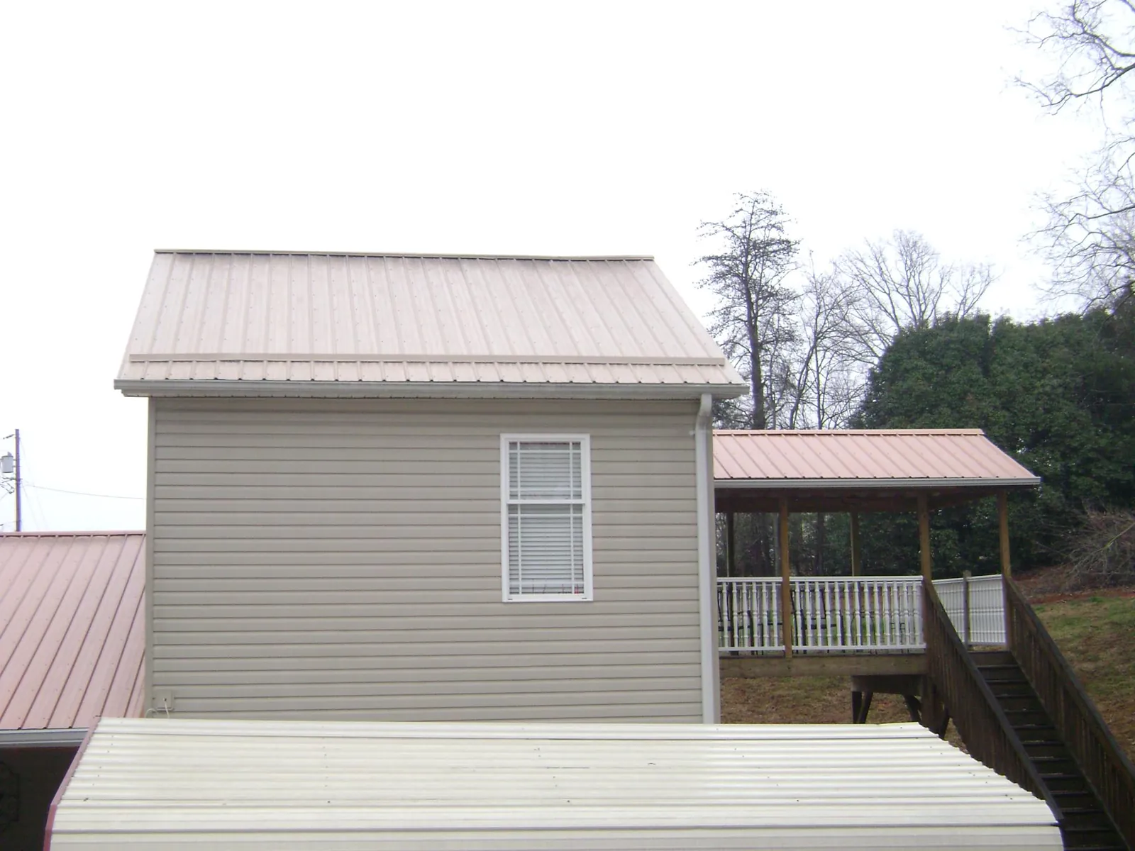 Tan metal roofs on a two story addition and attached porch, from a Roof Replacement job in Abrams